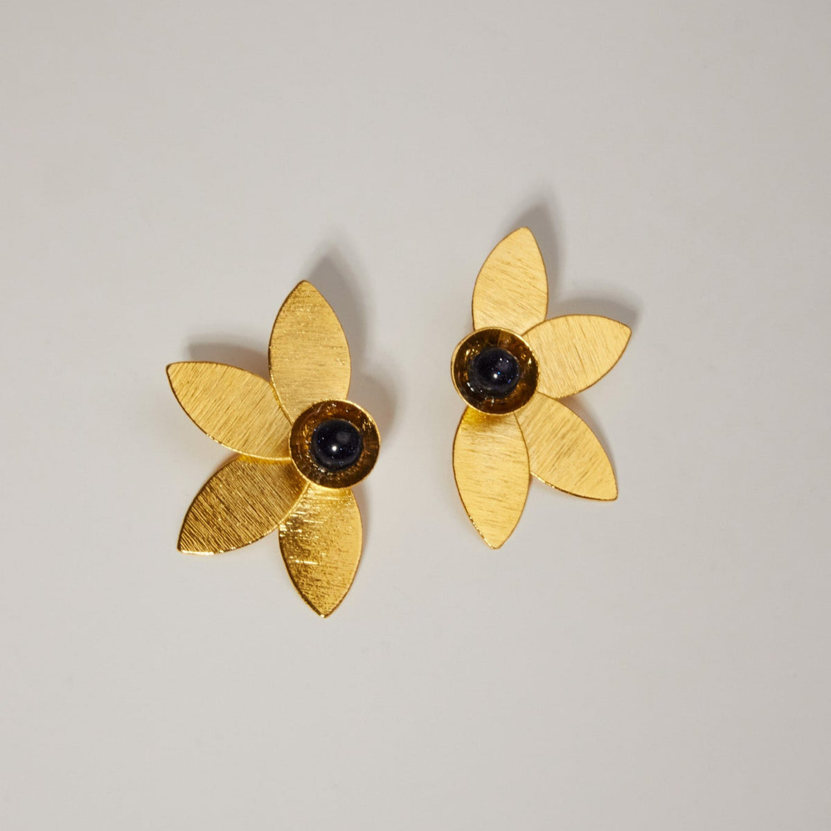 Gold flower-shaped earrings with deep navy stone centers on a light background