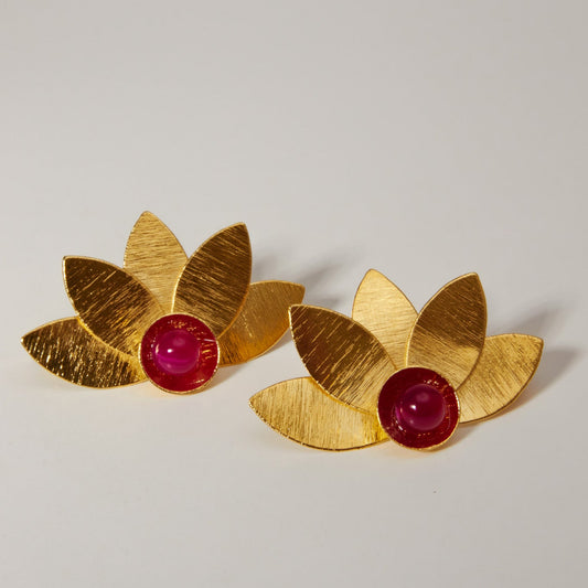 Gold leaf-shaped statement earrings with red stone centers on a light background
